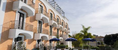 Un hotel con zona de piscina, incluyendo sillas de descanso y sombrillas, y un edificio con balcones.