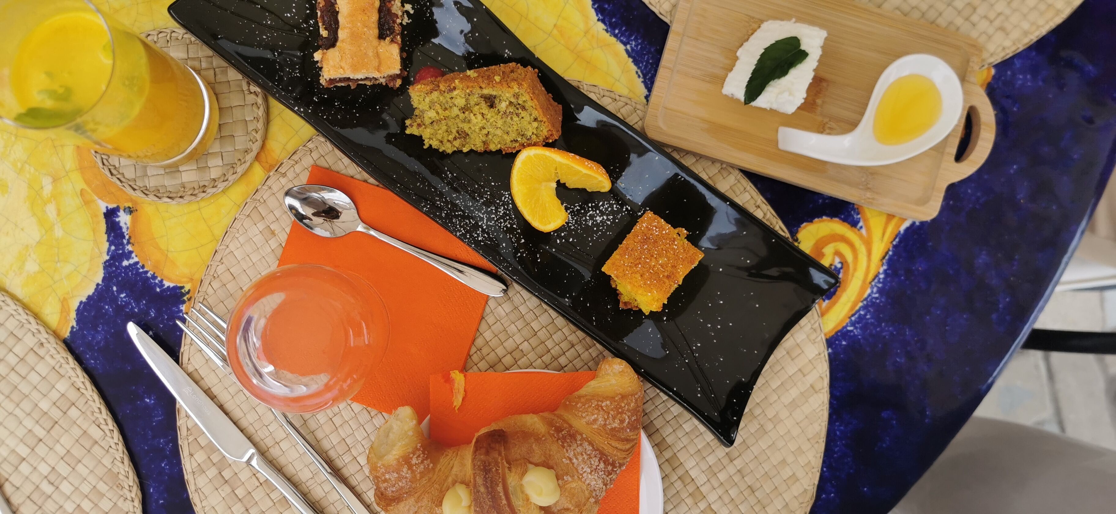 A breakfast setting with various pastries, a glass of orange juice, and a wooden board with a white object.