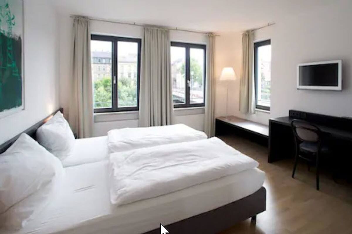 Ein Hotelzimmer mit einem großen Bett, einem Schreibtisch, einem Stuhl und einem Fernseher an der Wand.