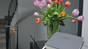 A clear view of a staircase with a metal railing, a glass vase with pink and red tulips, and a book titled "TANDEM" on a glass table. - Tandem (Bamberg)