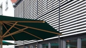 An outdoor seating area with tables and chairs, a large umbrella, and a potted plant.