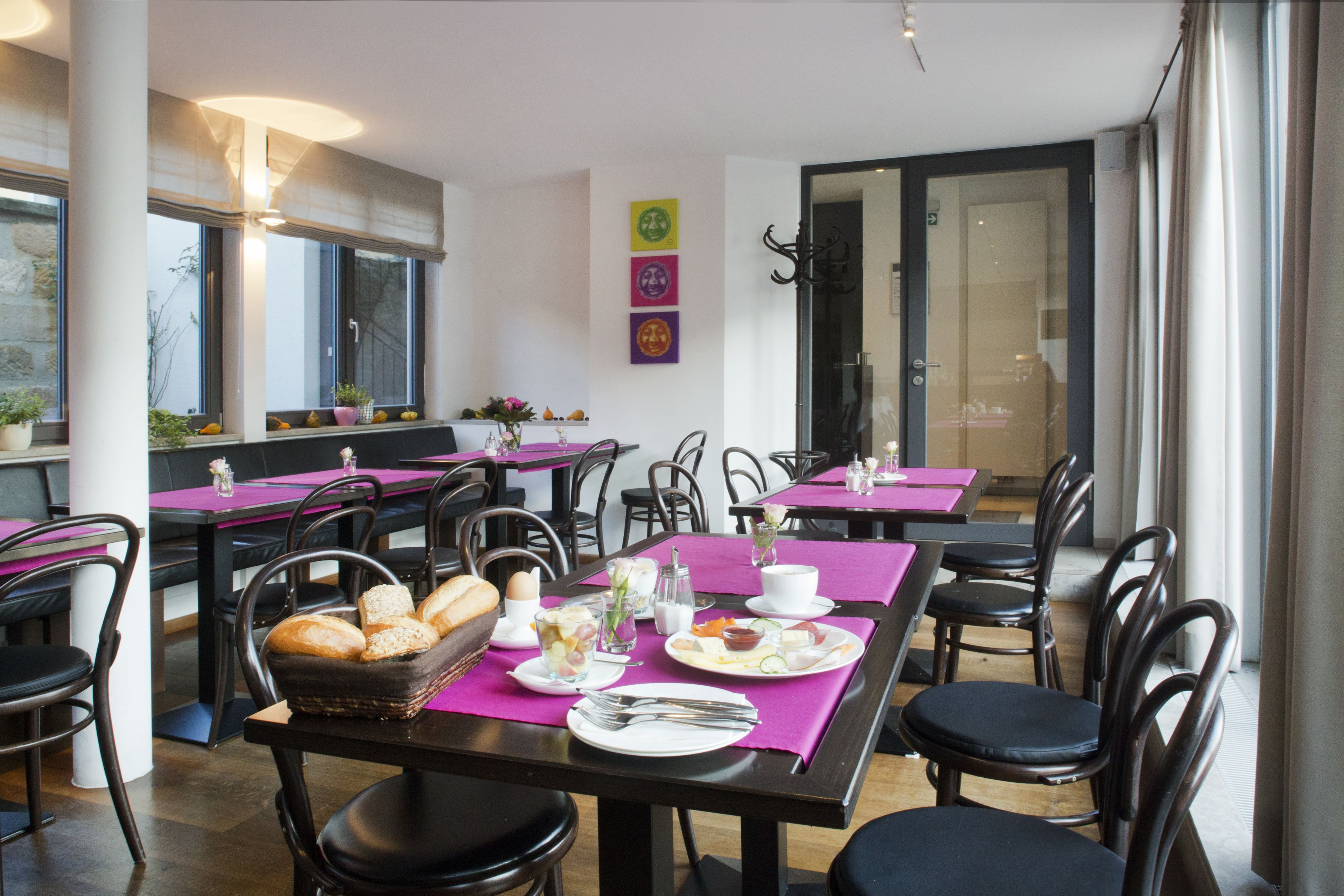 A restaurant with multiple tables and chairs, each set with plates, cutlery, and a basket of bread.
