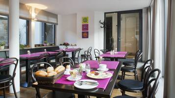 A restaurant with multiple tables and chairs, each set with plates, cutlery, and a basket of bread.