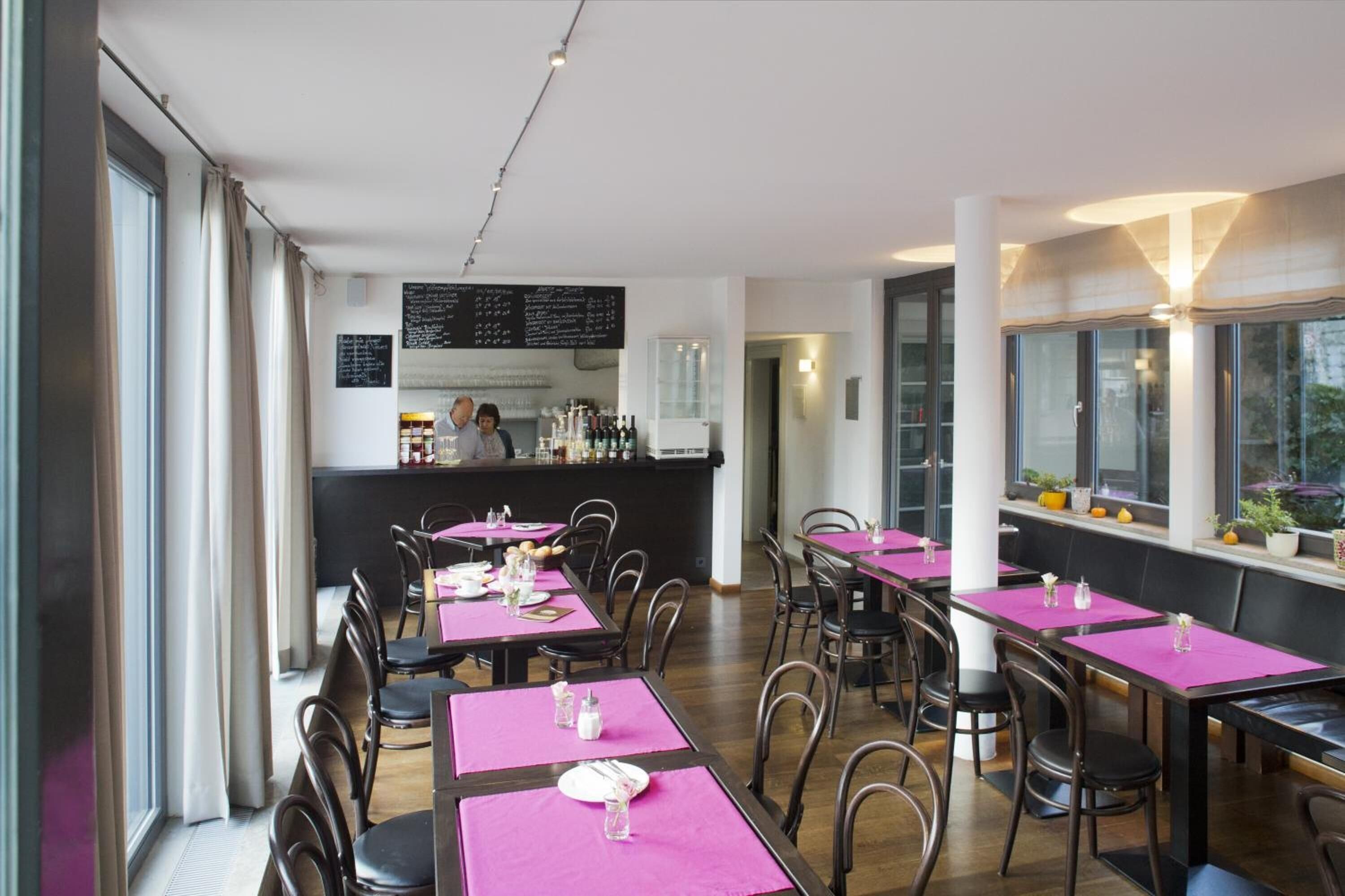 Un restaurant avec des tables dressées pour le service, un coin bar et un tableau affichant le menu.