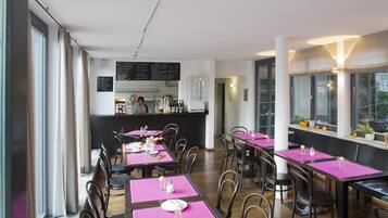 Un restaurant avec des tables dressées pour le service, un coin bar et un tableau affichant le menu.