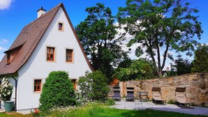 A white house with a brown roof, surrounded by greenery and stone walls. - Boutiquehotel Goldene Rose (Rothenburg ob der Tauber)