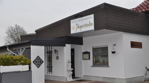 Ein Hotelrestaurant namens „Jägerstube“ mit weißer Fassade, schwarzem Markisenvorzelt und einem Schild.