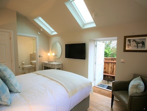 A bedroom with a large bed, a vanity with a mirror, a television on the wall, and a door leading to an outdoor area. - The White Horse Inn (Pulborough)