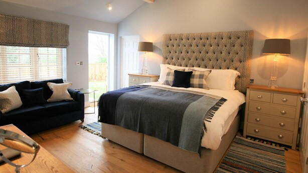 A bedroom with a bed, bedside tables, a sofa, and a window with blinds. - The White Horse Inn (Pulborough)