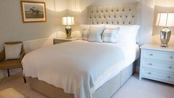 A neatly arranged bedroom with a large bed, a bedside table with lamps, a chair, and a framed picture on the wall.