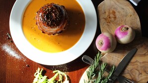 A plate with a meat dish and a side of soup, accompanied by two turnips and some herbs on a wooden board. - The White Horse Inn (Pulborough)
