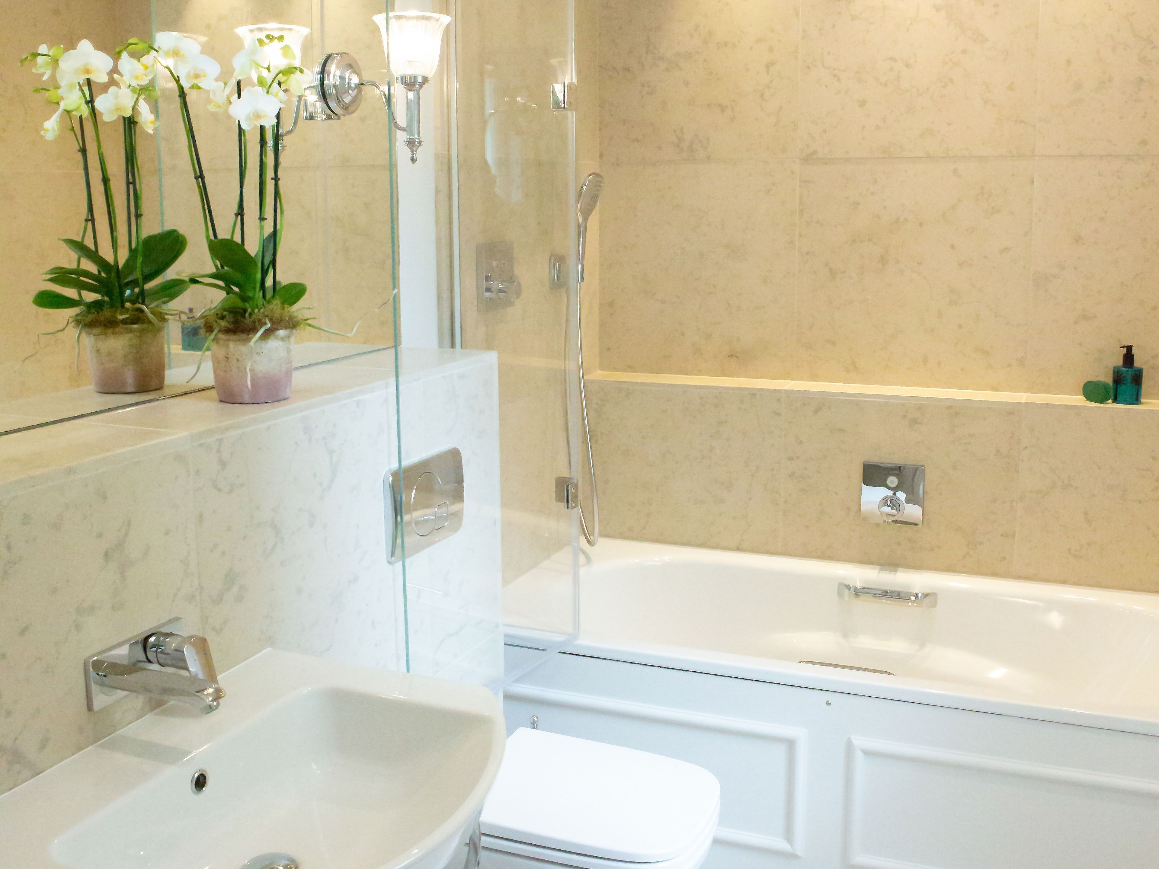A bathroom with a white bathtub, a sink, and a toilet. There are potted plants on the counter and a shower area with a glass door.