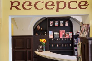 A reception area with a 'reception' sign above, a counter with a vase of flowers, and a bookshelf with books and keychains. - Pension U Lilie (Prague)