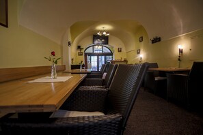 A restaurant with a long wooden table, wicker chairs, and a vase with a red rose. - Pension U Lilie (Prague)