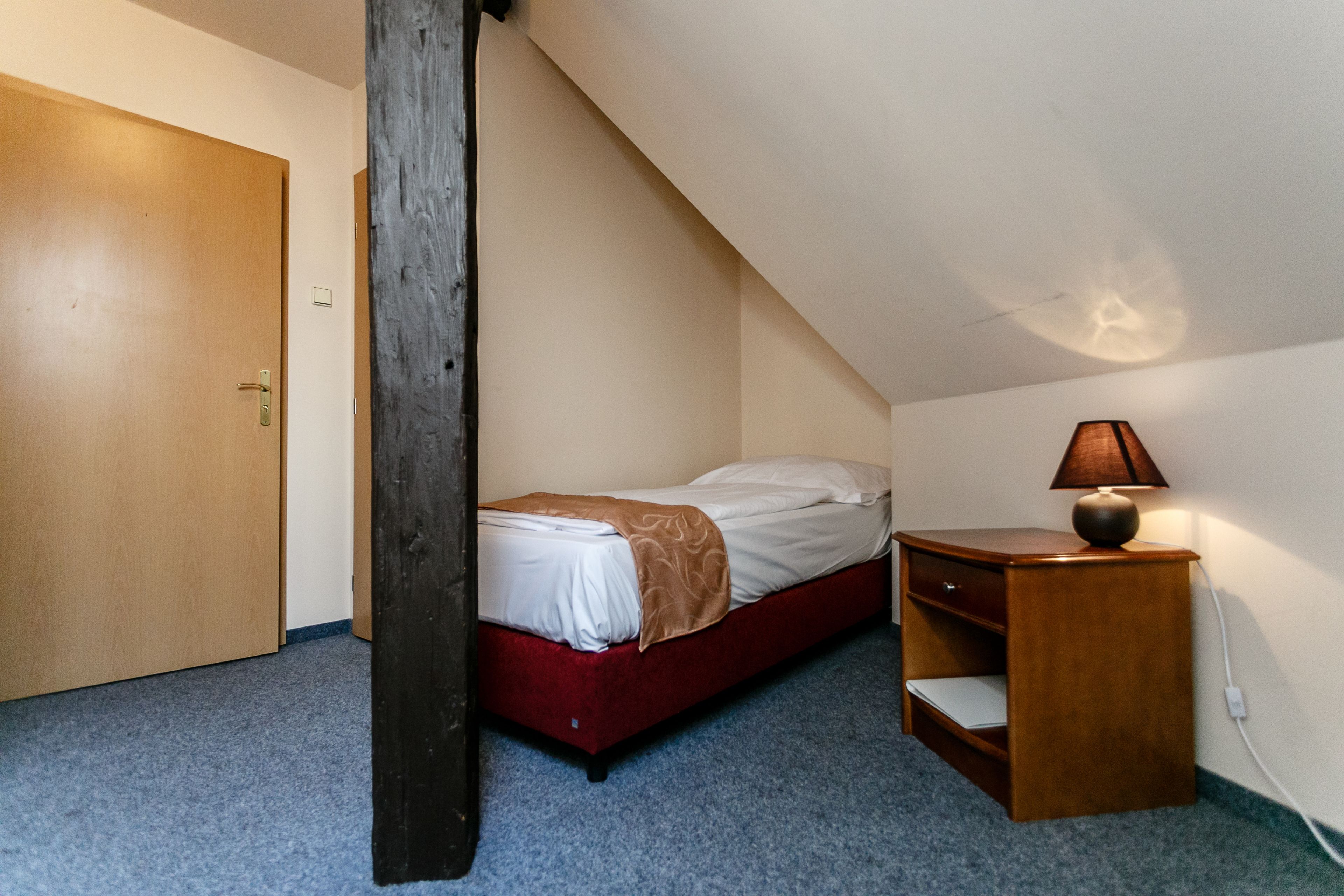 A small, single-bed room with a wooden desk and a lamp.