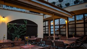 An outdoor patio with wooden tables and chairs, a covered seating area, and a staircase leading to an upper level. - Pension U Lilie (Prague)
