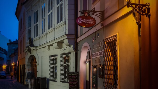A street view at dusk with a building featuring a sign for 'Budweiser Outdoor' and a restaurant named 'Pension Restaurant'. - Pension U Lilie (Prague)