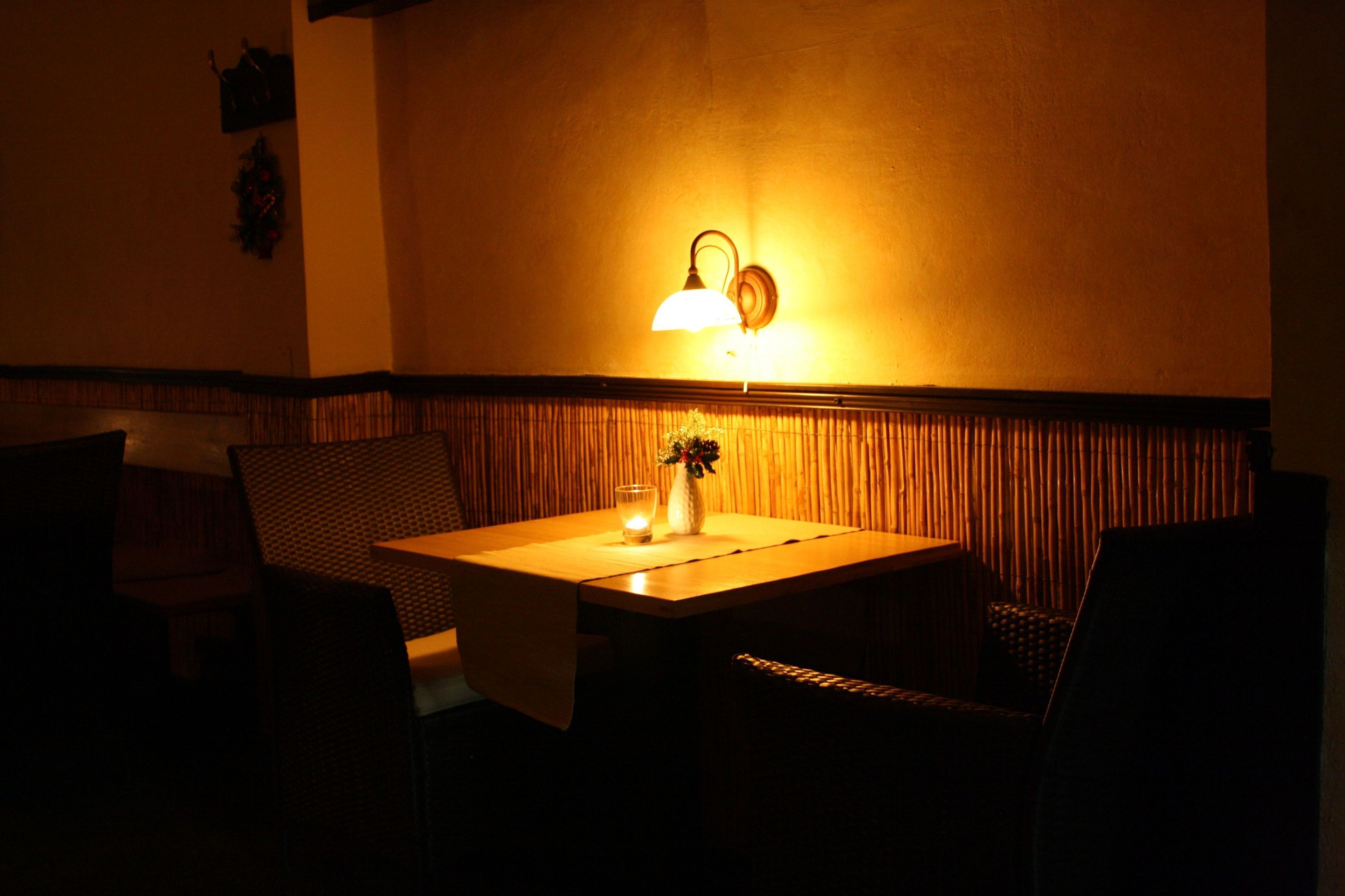 Ein schwach beleuchtetes Restaurant mit Tisch und Stühlen, einer Wandleuchte und einem dekorativen Wandbild.