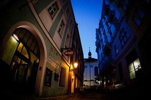 A narrow street with buildings on either side, a sign for a restaurant, and a car parked on the right. - Pension U Lilie (Prague)
