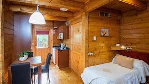 A wooden cabin with a dining area, kitchenette, and a bed with a red headboard. - Accommodation de Salut Somlom (Sant Esteve de Palautordera)