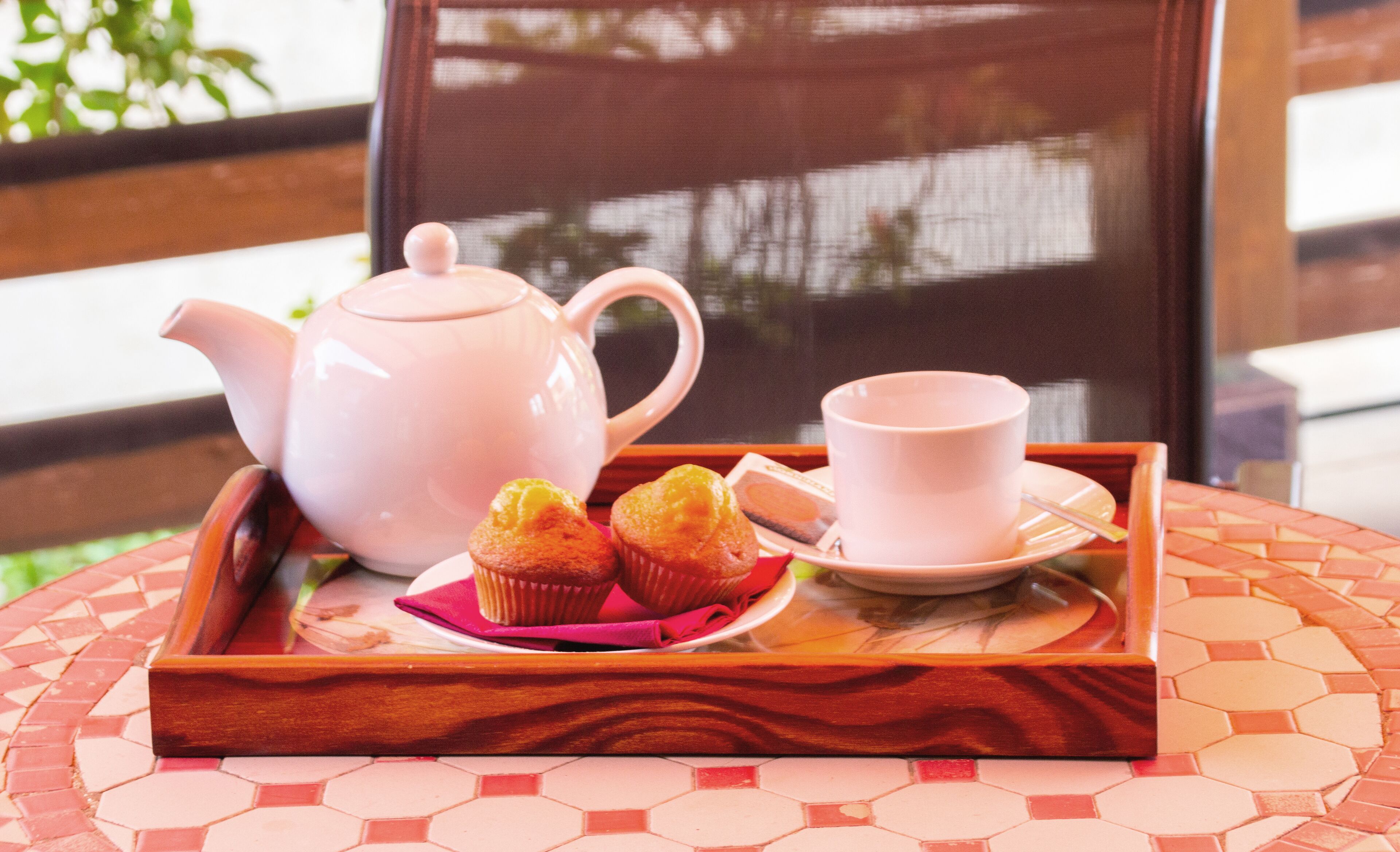 Una bandeja con un ramillete de té, una taza y muffins sobre una mesa con un patrón de baldosas hexagonales.