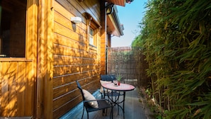 A wooden cabin with a patio area featuring a table and chairs, a window, and a bamboo fence. - Accommodation de Salut Somlom (Sant Esteve de Palautordera)