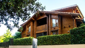 A wooden cabin with a balcony, surrounded by a well-maintained hedge and a concrete wall. - Accommodation de Salut Somlom (Sant Esteve de Palautordera)