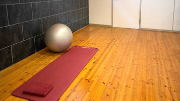 Una habitación con piso de madera, una colchoneta roja de ejercicio y una pelota grande de gimnasia.