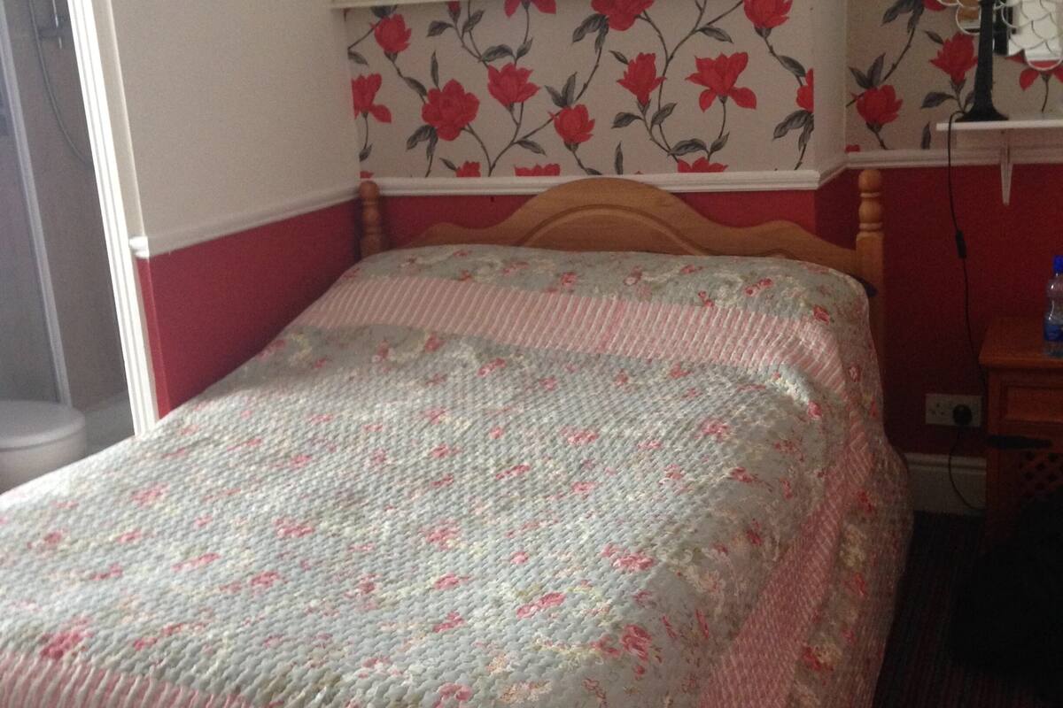 A bedroom with a bed, a mirror, a television, and floral wallpaper.