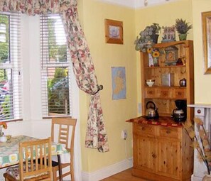 A room with a wooden cabinet, a table with chairs, and a window with blinds. - Acara House (Dublin)