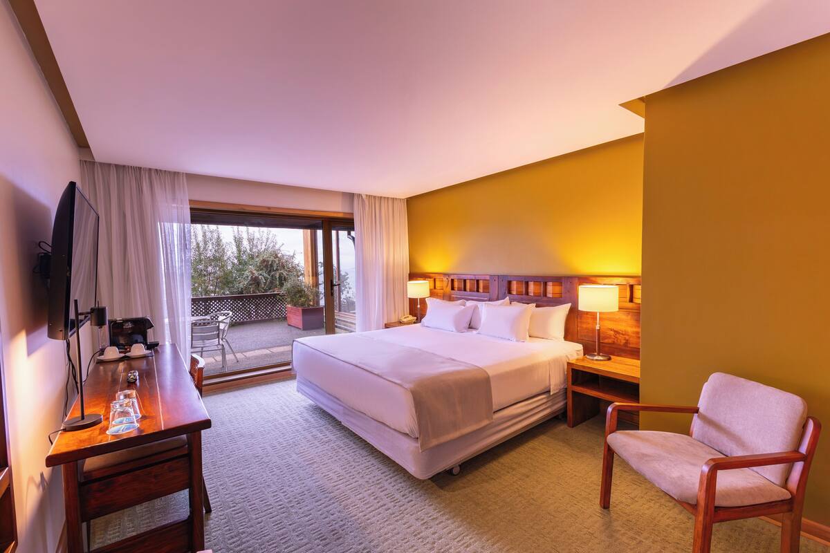 A hotel room with a bed, a desk with a computer, a chair, a TV, and a balcony with a view.