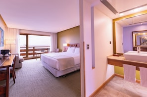 A hotel room with a bed, desk, chair, and a bathroom with a sink and mirror. - Wyndham Puerto Varas Pettra (Puerto Varas)
