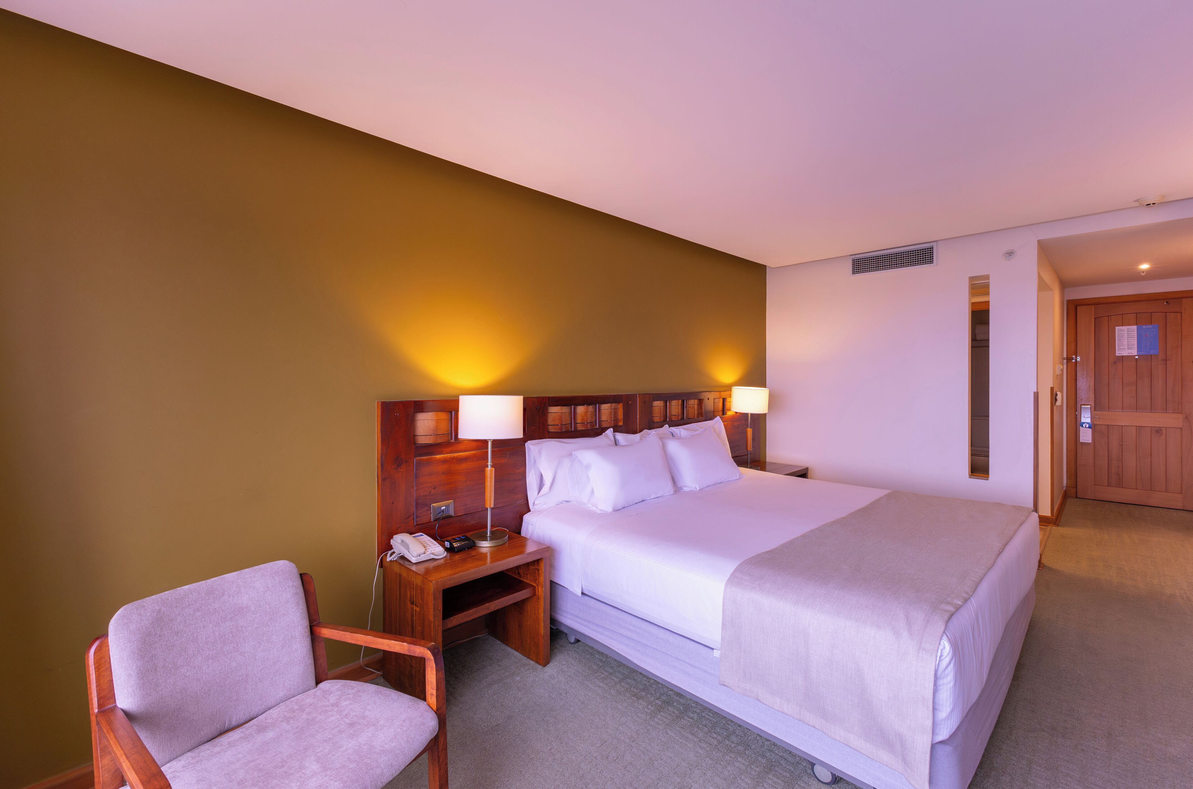 Una habitación de hotel con cama, mesitas de noche, una silla y una puerta.