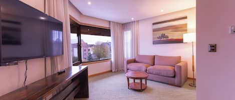 A modern living room with a flat-screen TV, a sofa, a coffee table, and a large window.