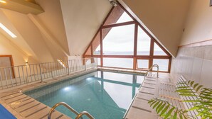Una piscina interior con vista al mar, techo alto y suelo de baldosas.