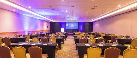 A conference room with tables, chairs, a stage, and a presentation screen at Wyndham Petra Hotels.