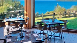 Un restaurante con mesas preparadas para comer, vista al mar y una montaña en la distancia.