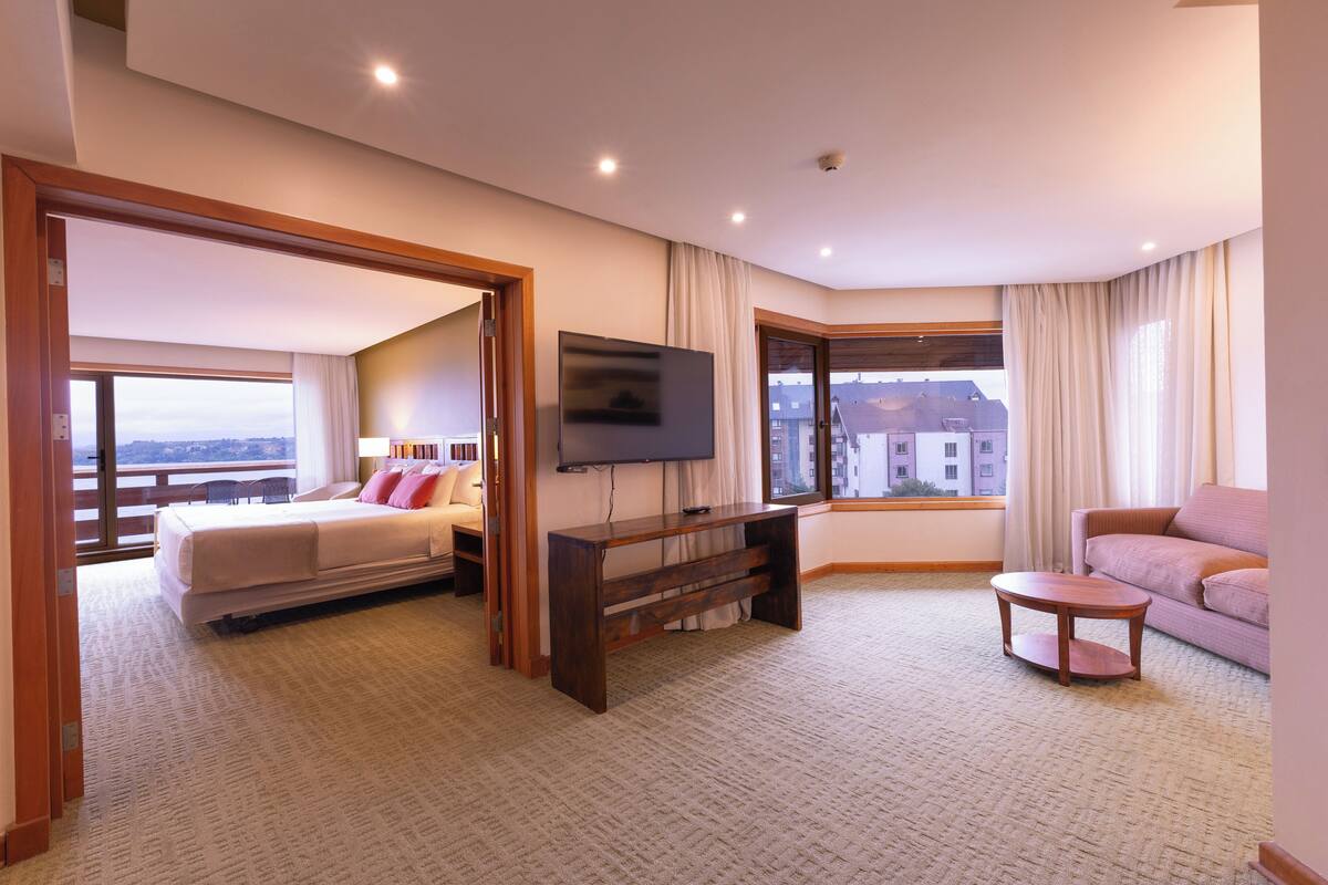 A hotel room with a bed, a TV, a sofa, a small table, and a large window with a view.