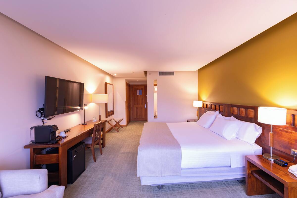 A hotel room with a bed, desk, chair, TV, and lamps.