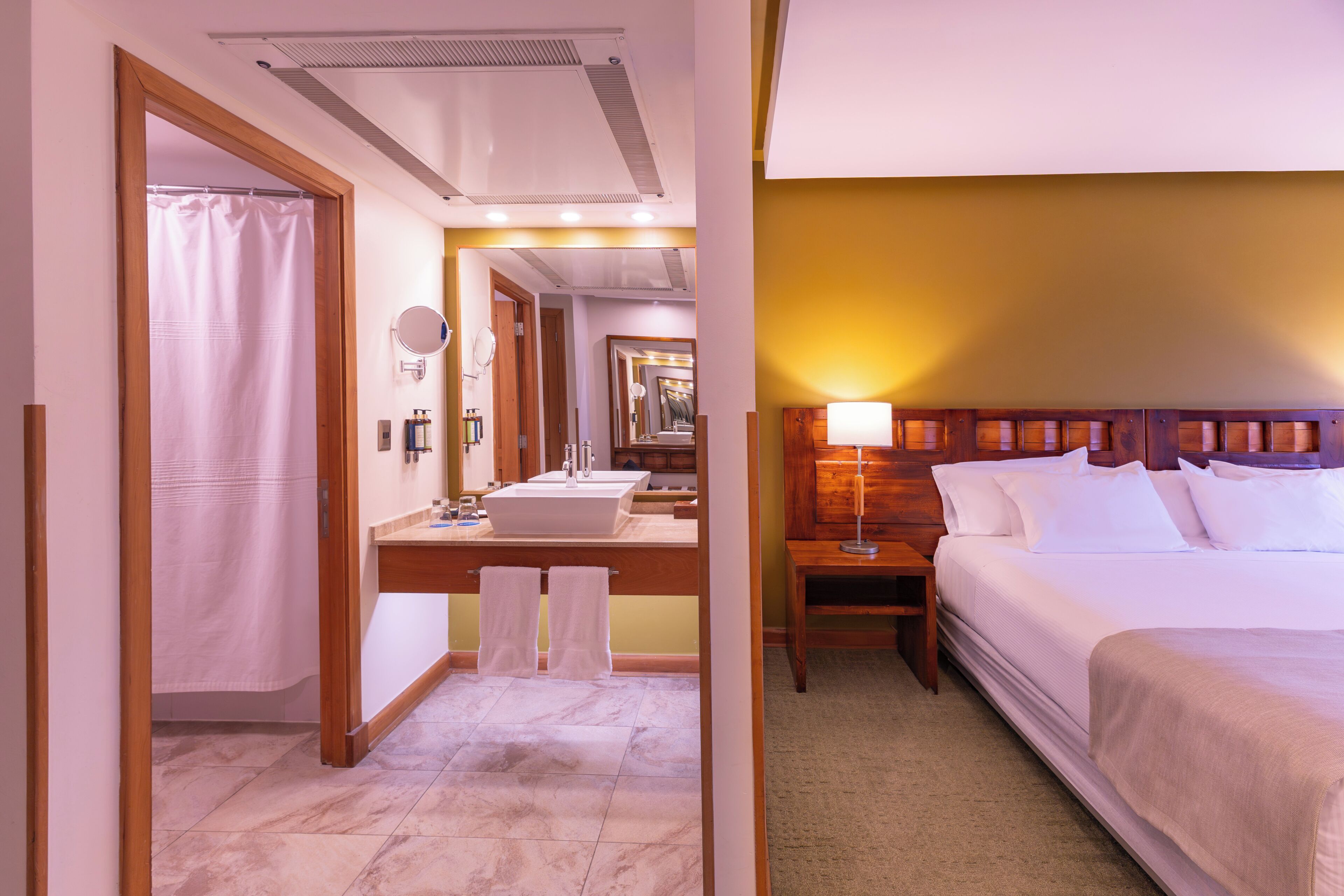 A hotel room with a bathroom, a bed, a nightstand, and a mirror.