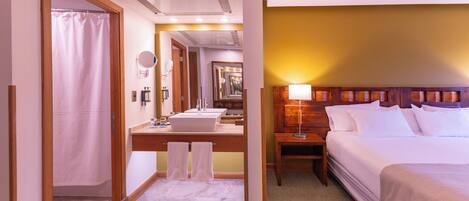 A hotel room with a bathroom, a bed, a nightstand, and a mirror.