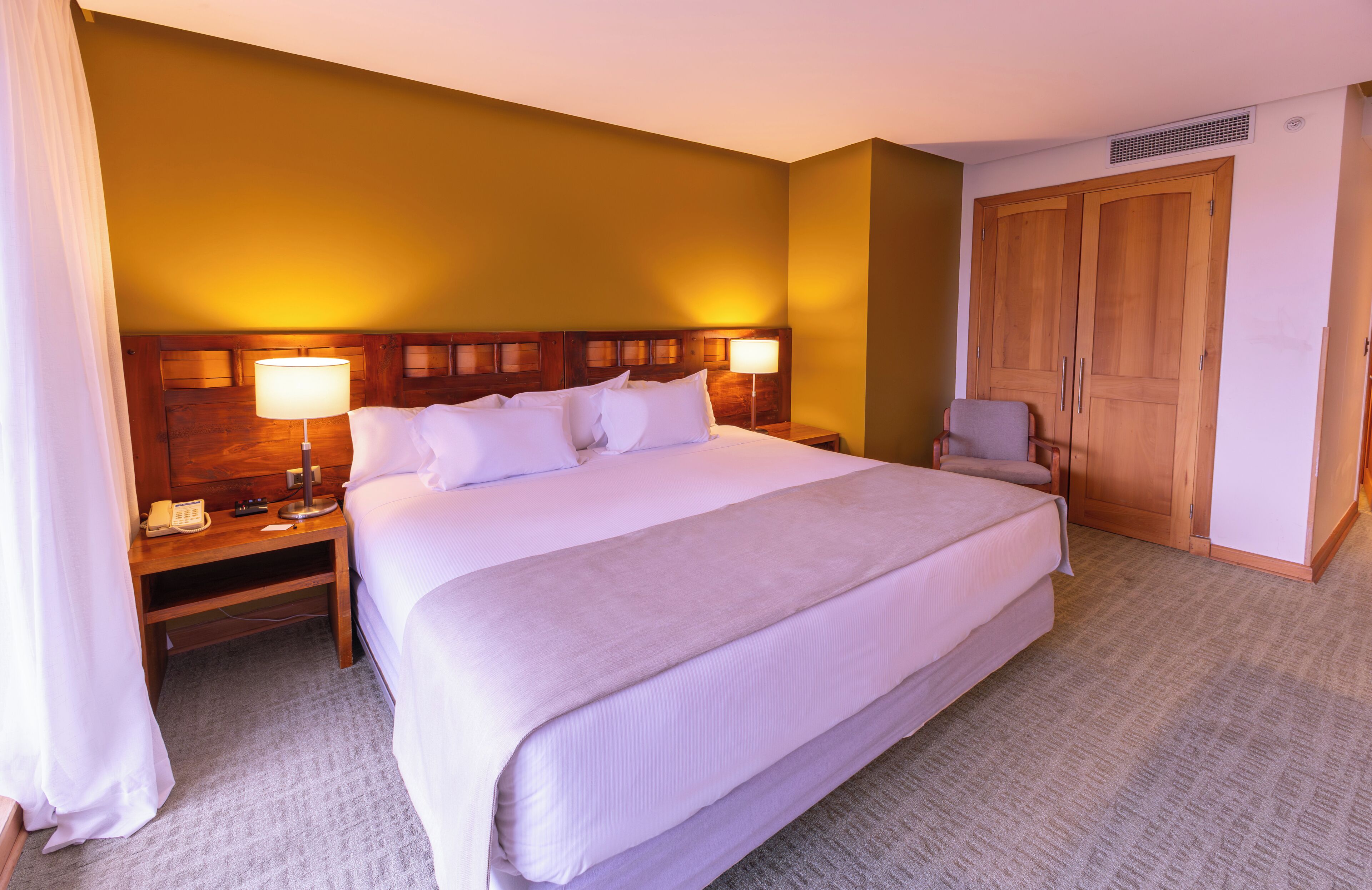 A hotel room with a large bed, bedside lamps, a wooden wardrobe, and a telephone on the nightstand.