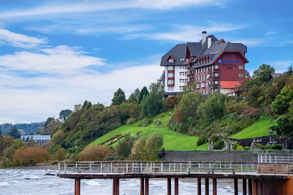 A hotel with a red and white facade, multiple balconies, and a view of a river. - Wyndham Puerto Varas Pettra (Puerto Varas)
