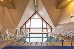 An indoor swimming pool with a view of the sea, a wooden deck, and a high ceiling. - Wyndham Puerto Varas Pettra (Puerto Varas)