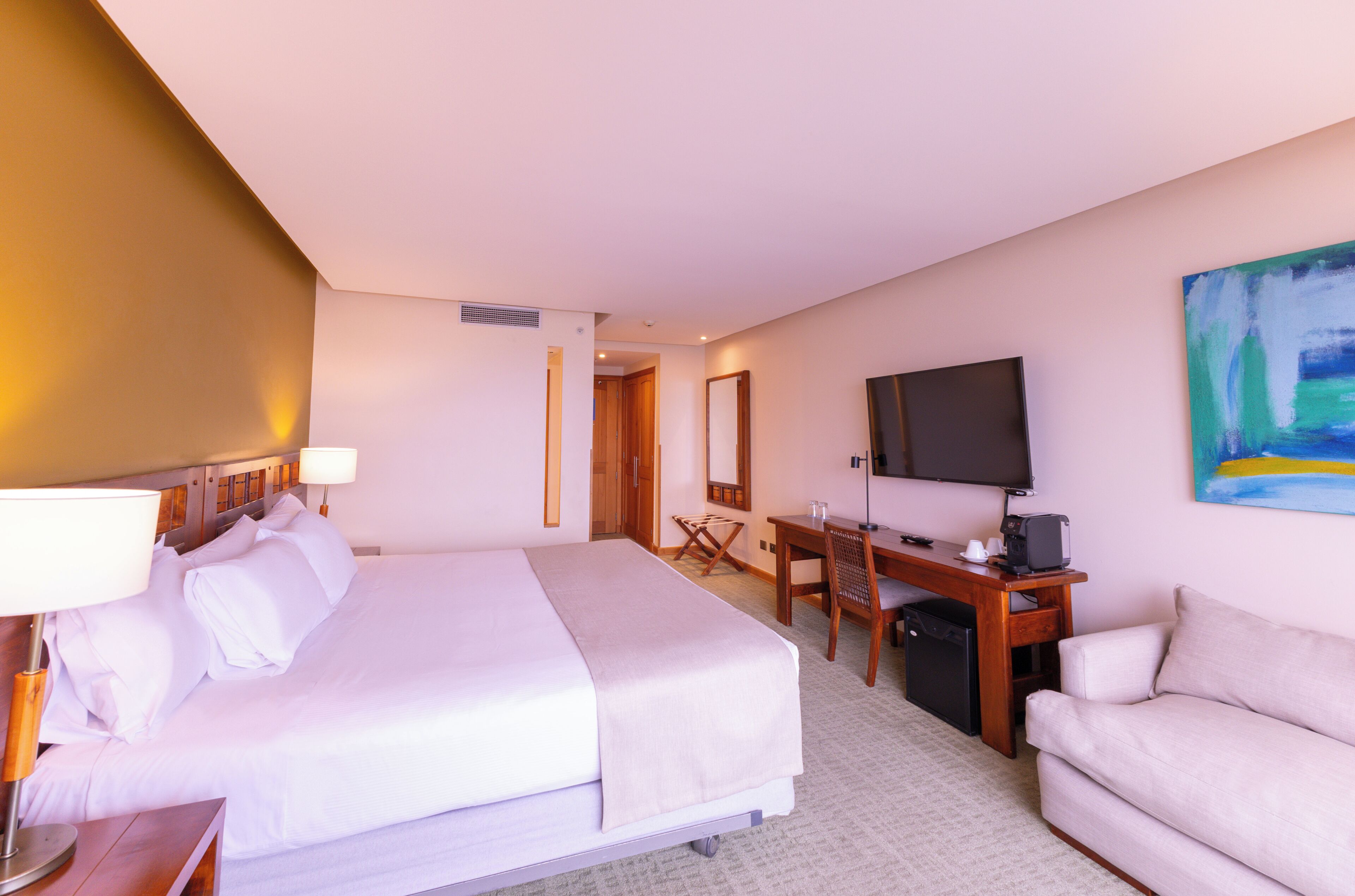 A hotel room with a bed, desk, chair, TV, and a couch.