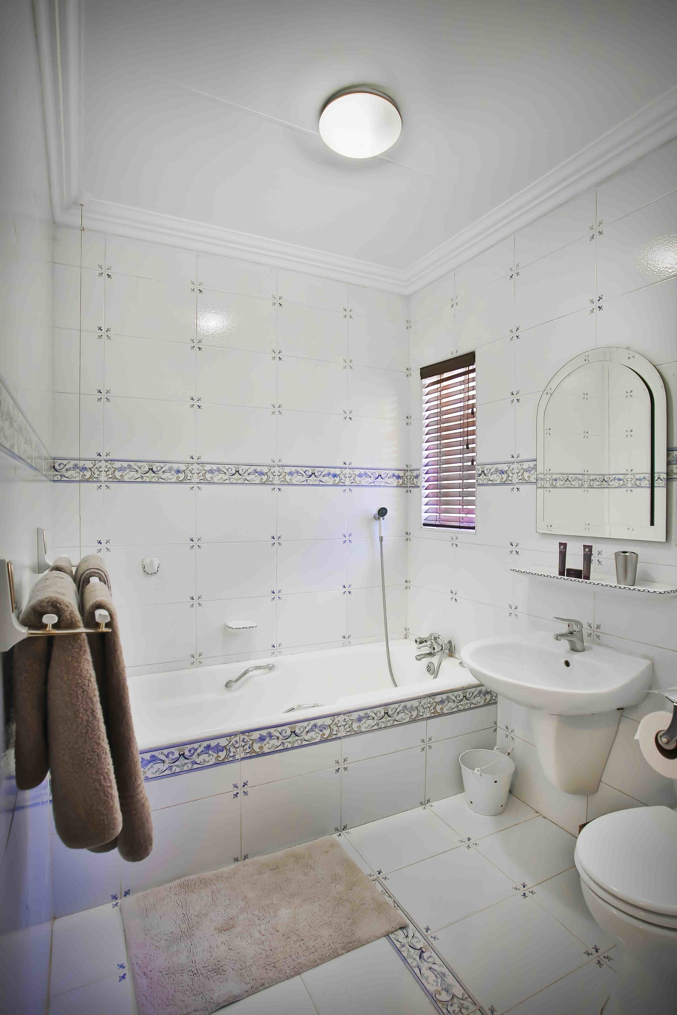 Casa de banho com banheira, pia e sanita, com azulejos brancos e uma moldura decorativa, e uma janela com persianas.