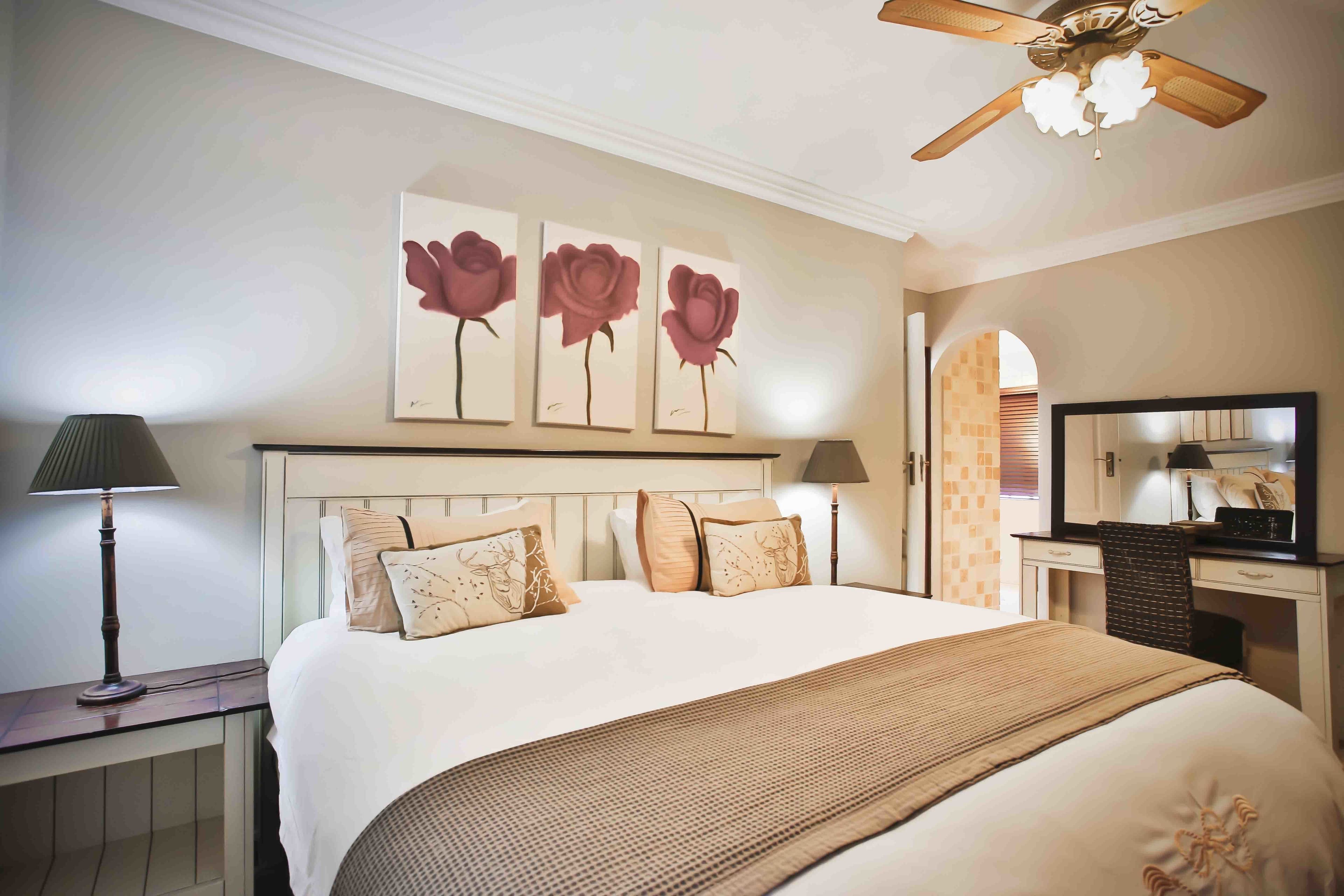 Une chambre d’hôtel avec un grand lit, un bureau avec une chaise, un ventilateur de plafond et des œuvres d’art accrochées au mur.