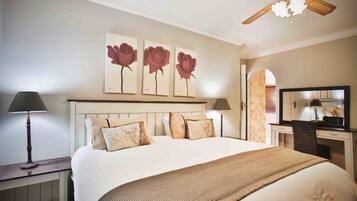 Une chambre d’hôtel avec un grand lit, un bureau avec une chaise, un ventilateur de plafond et des œuvres d’art accrochées au mur.