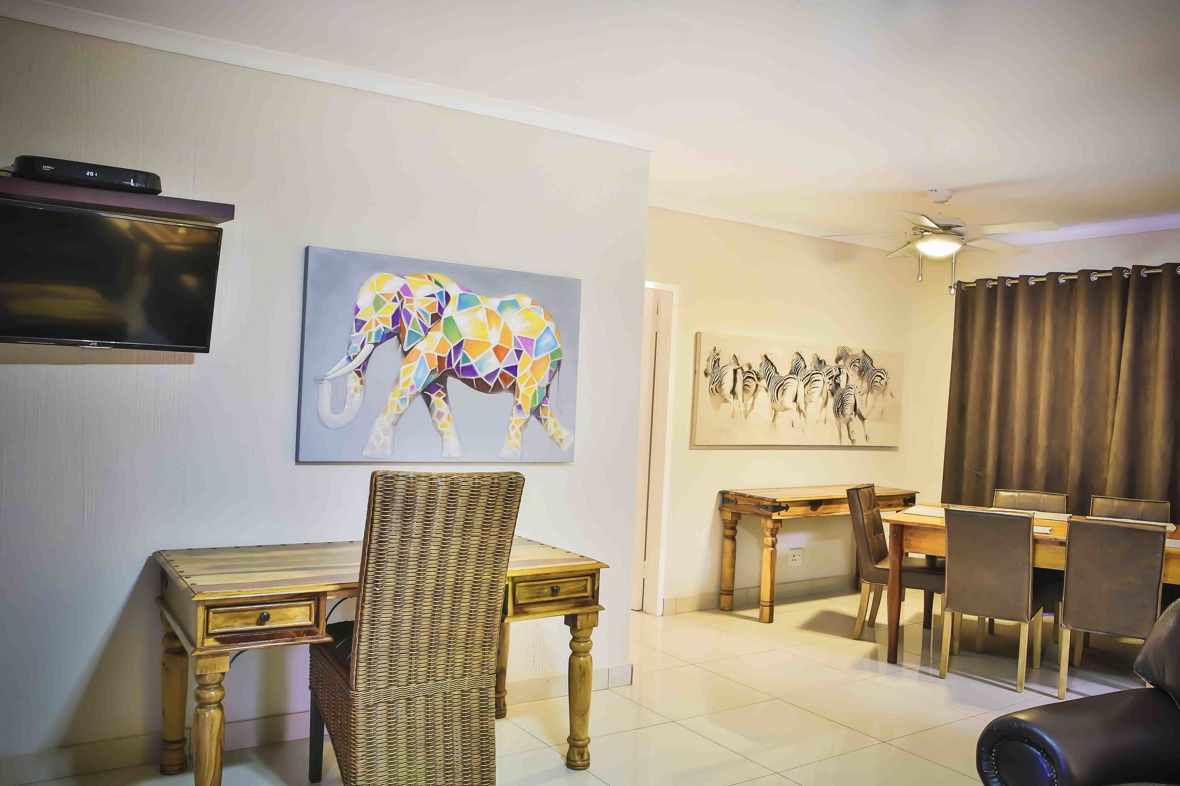 Een woonkamer met een televisie, een eethoek met een tafel en stoelen, en kunstwerken aan de muur.