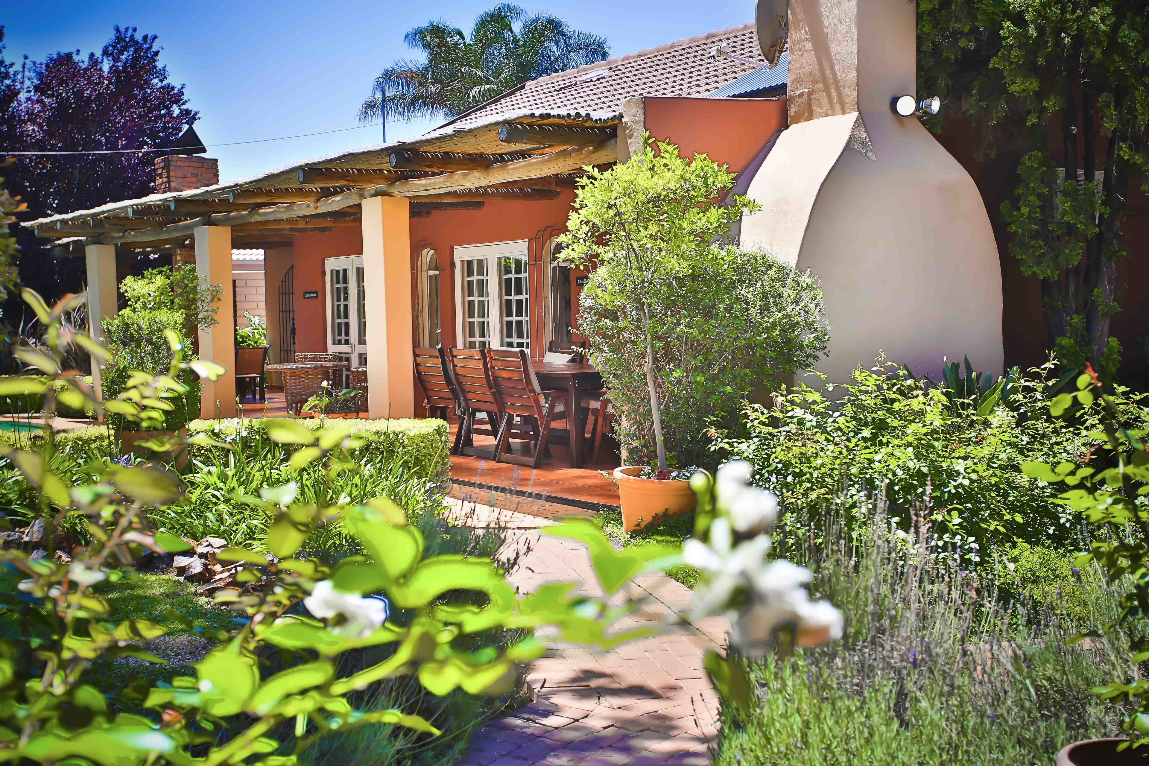 Una casa con un patio, un comedor con sillas y un jardín con diversas plantas.